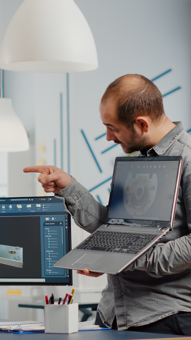 Man project supervisor holding laptop and pointing on display showing to woman industrial engineer who works on computer the development of new machinery prototype. Team working in creative office